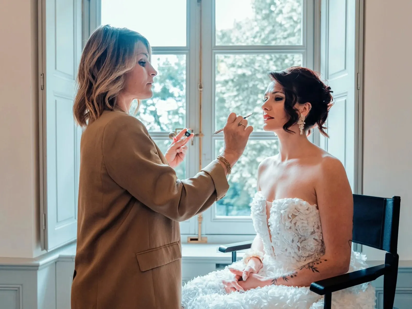 Mise en beauté de la mariée devant une fenêtre, au château