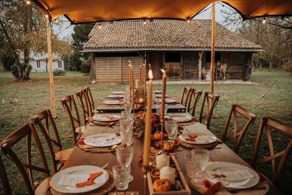 Longue table en bois sous la tente, bougies, citrouilles et serviettes orange