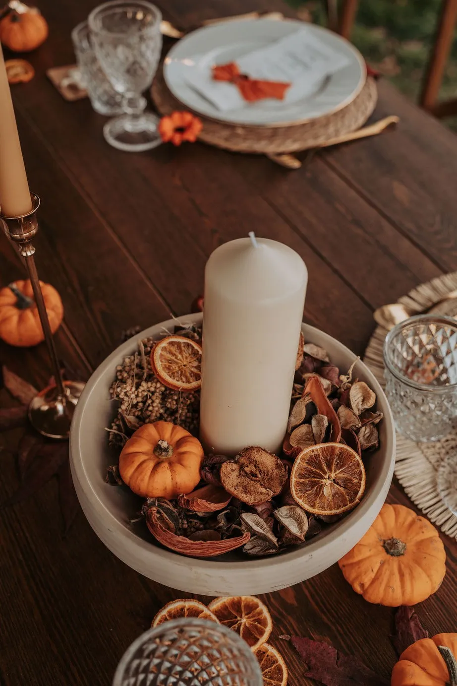 Bougie blanche dans une coupe de mini citrouilles et d'oranges séchées