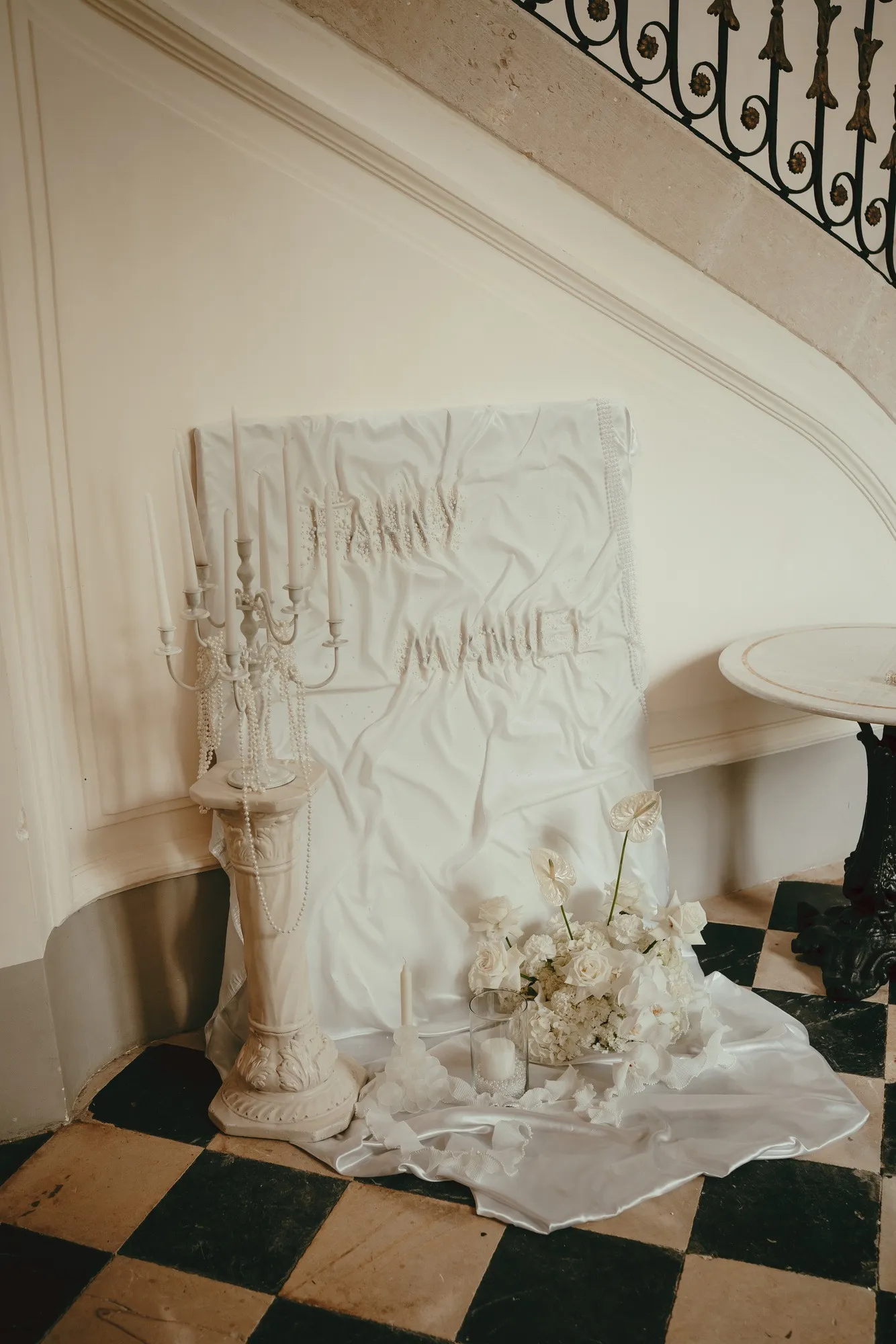 Tenture blanche brodée des prénoms des mariés, chandelier et fleurs blanches