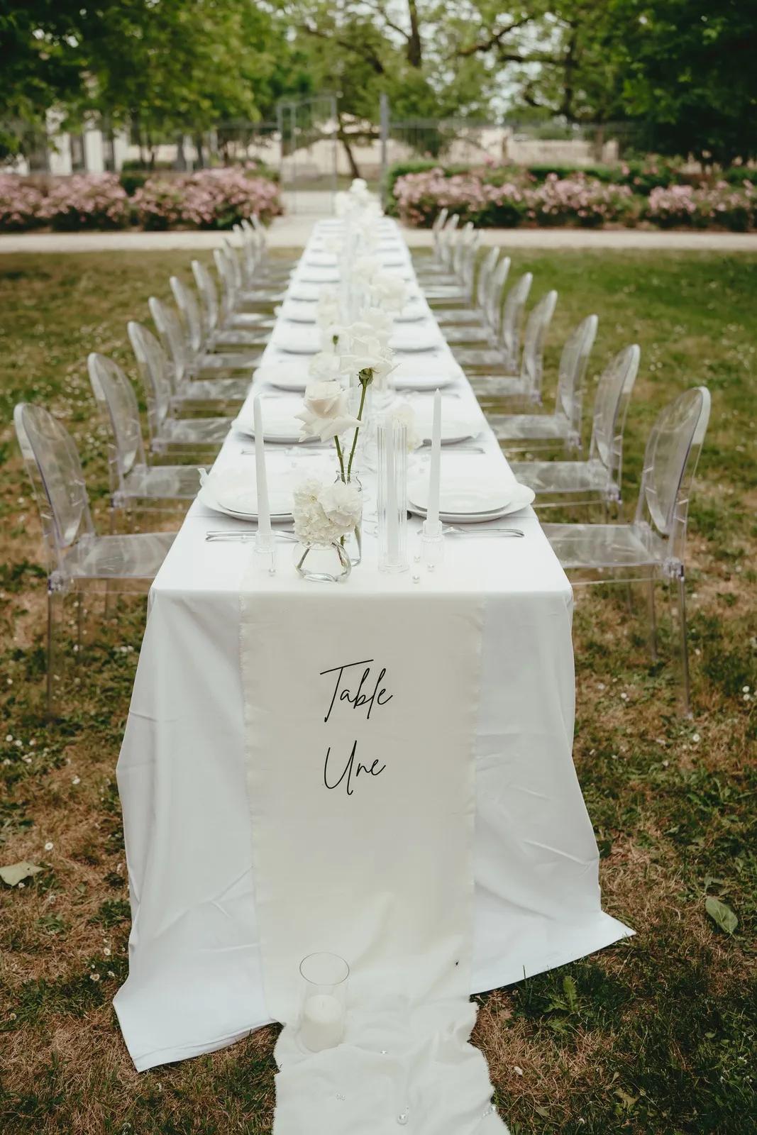 Longue table de mariage dressée en plein air, nappes blanches et chaises transparentes
