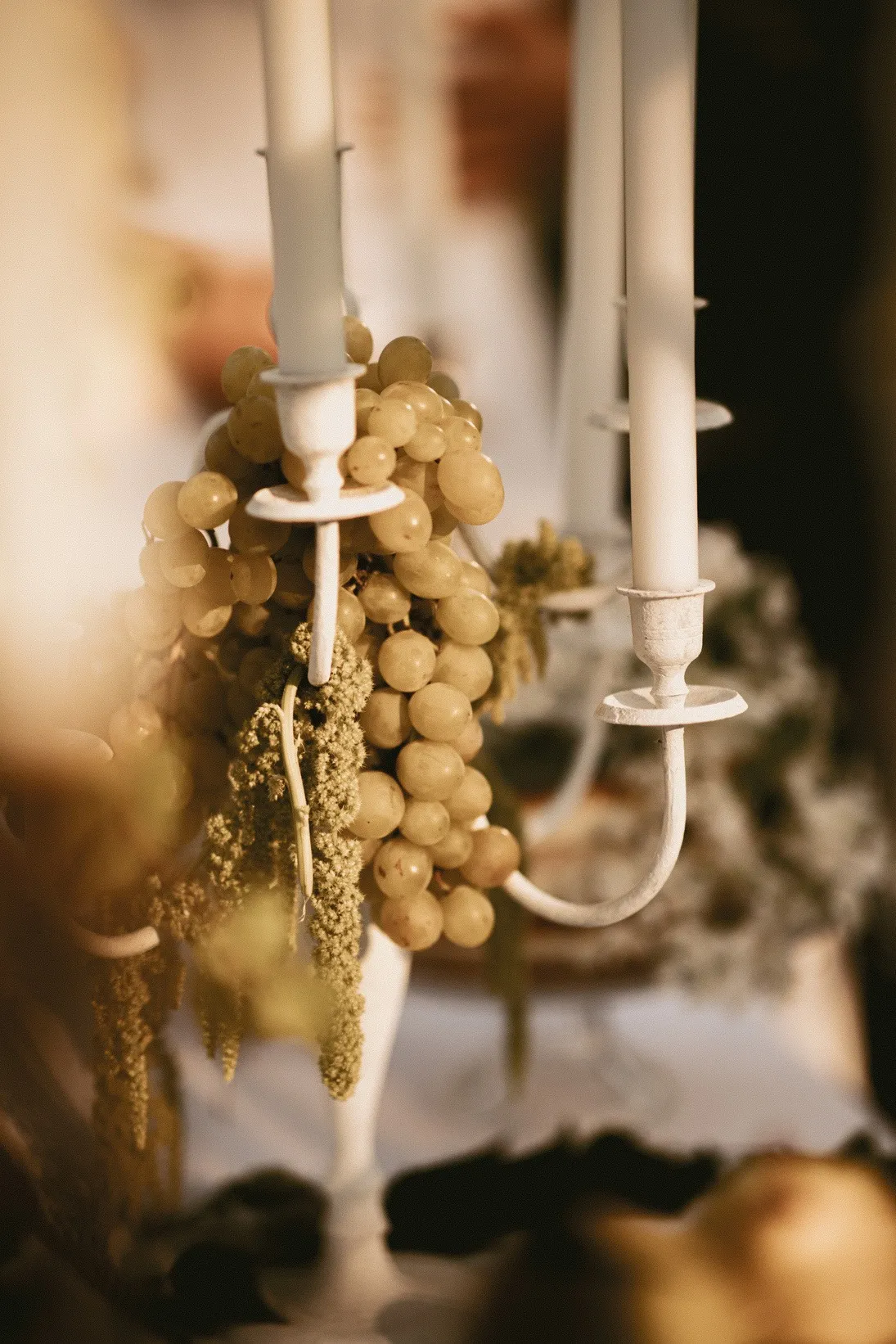 Chandelier blanc garni de grappes de raisin et de bougies, dans une lumière dorée