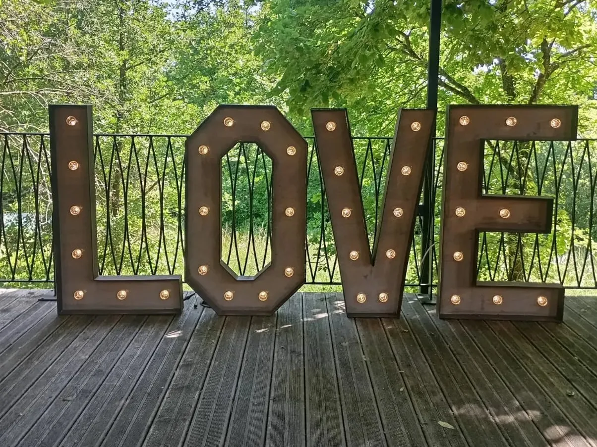 Les lettres LOVE en bois cerclé de métal, ampoules allumées, sur une terrasse en bois