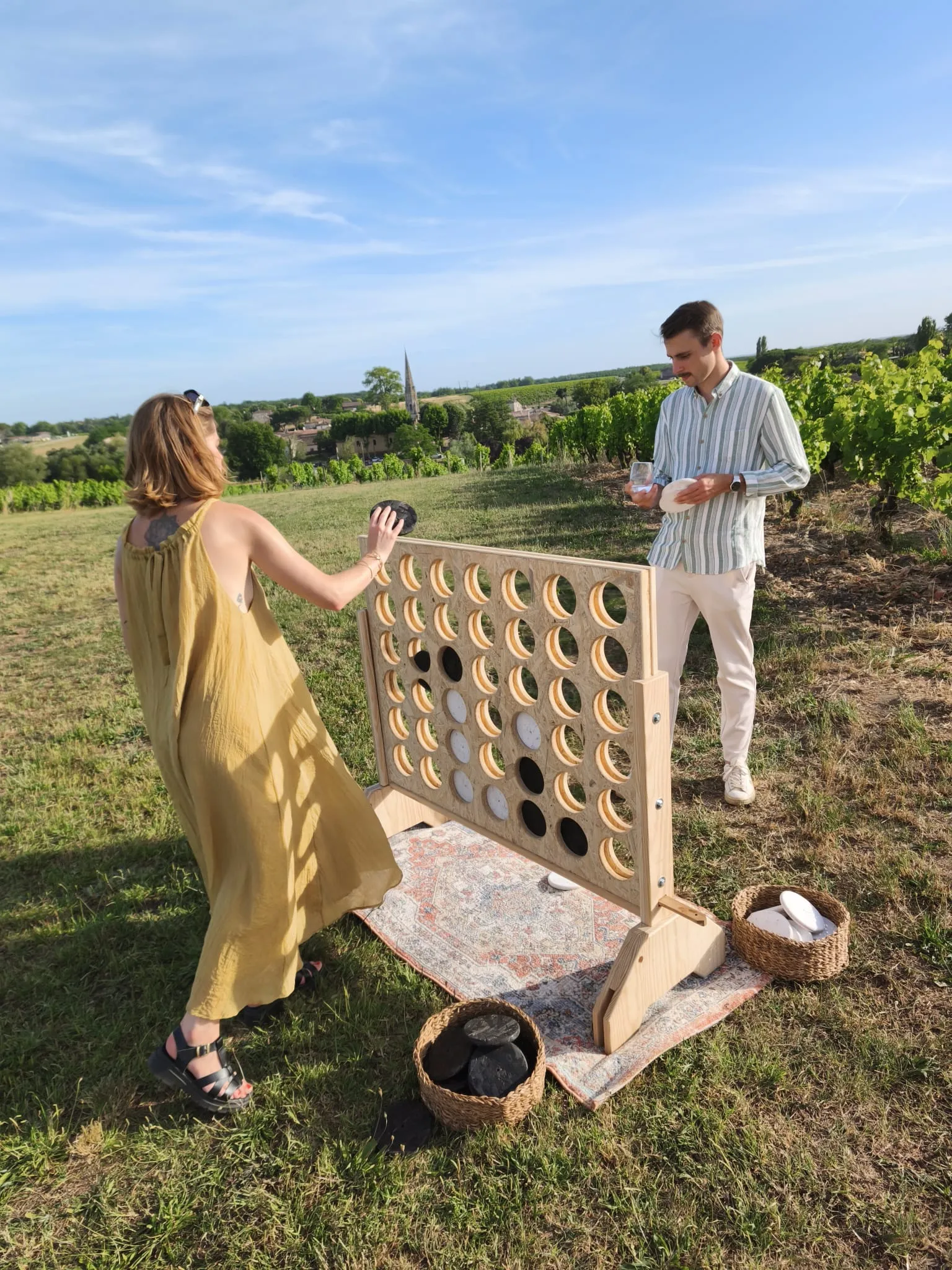 Puissance 4 géant en bois posé sur un tapis, face aux vignes