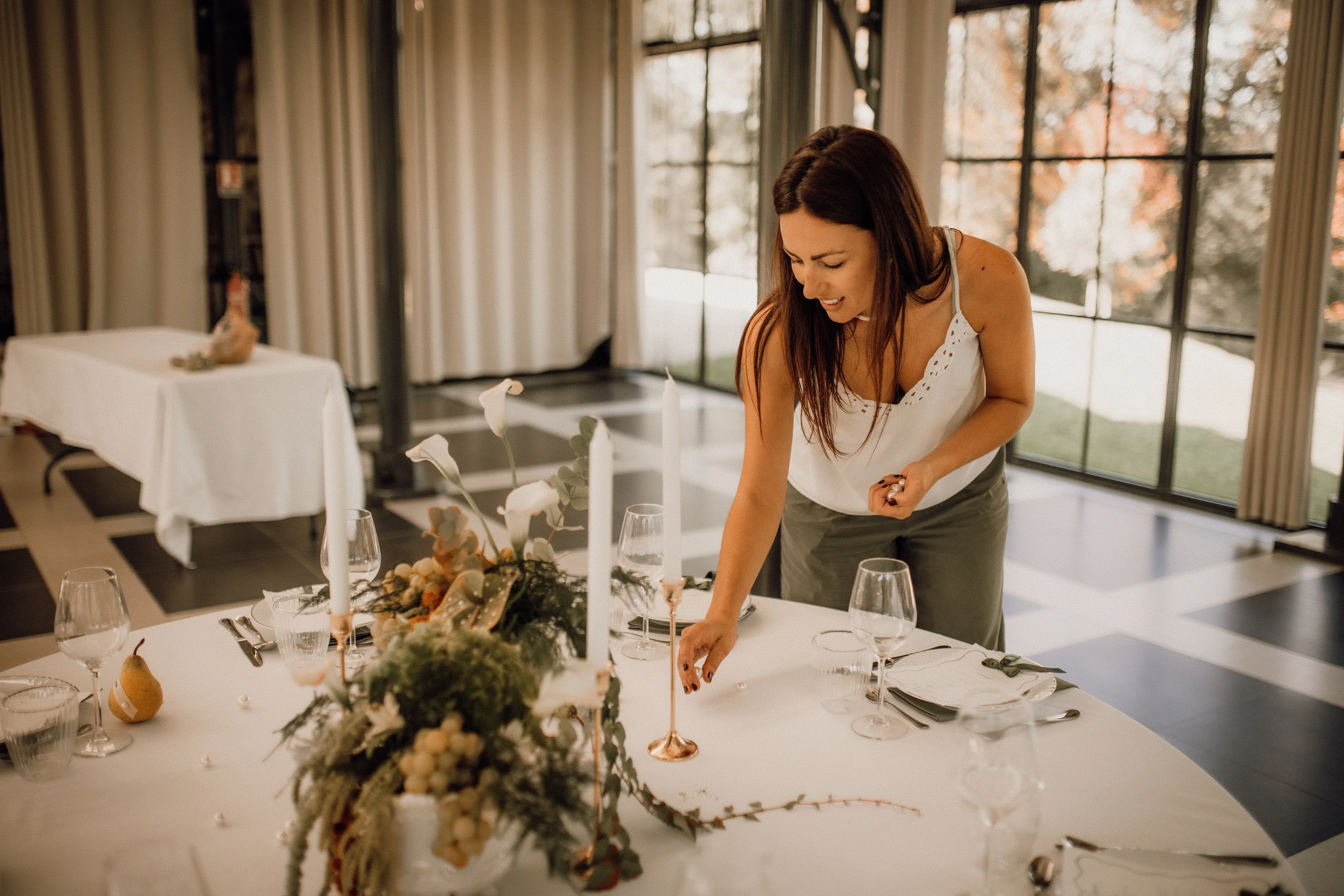 Ornella dresse une table de mariage : elle ajuste un bougeoir doré au milieu des raisins et des fleurs