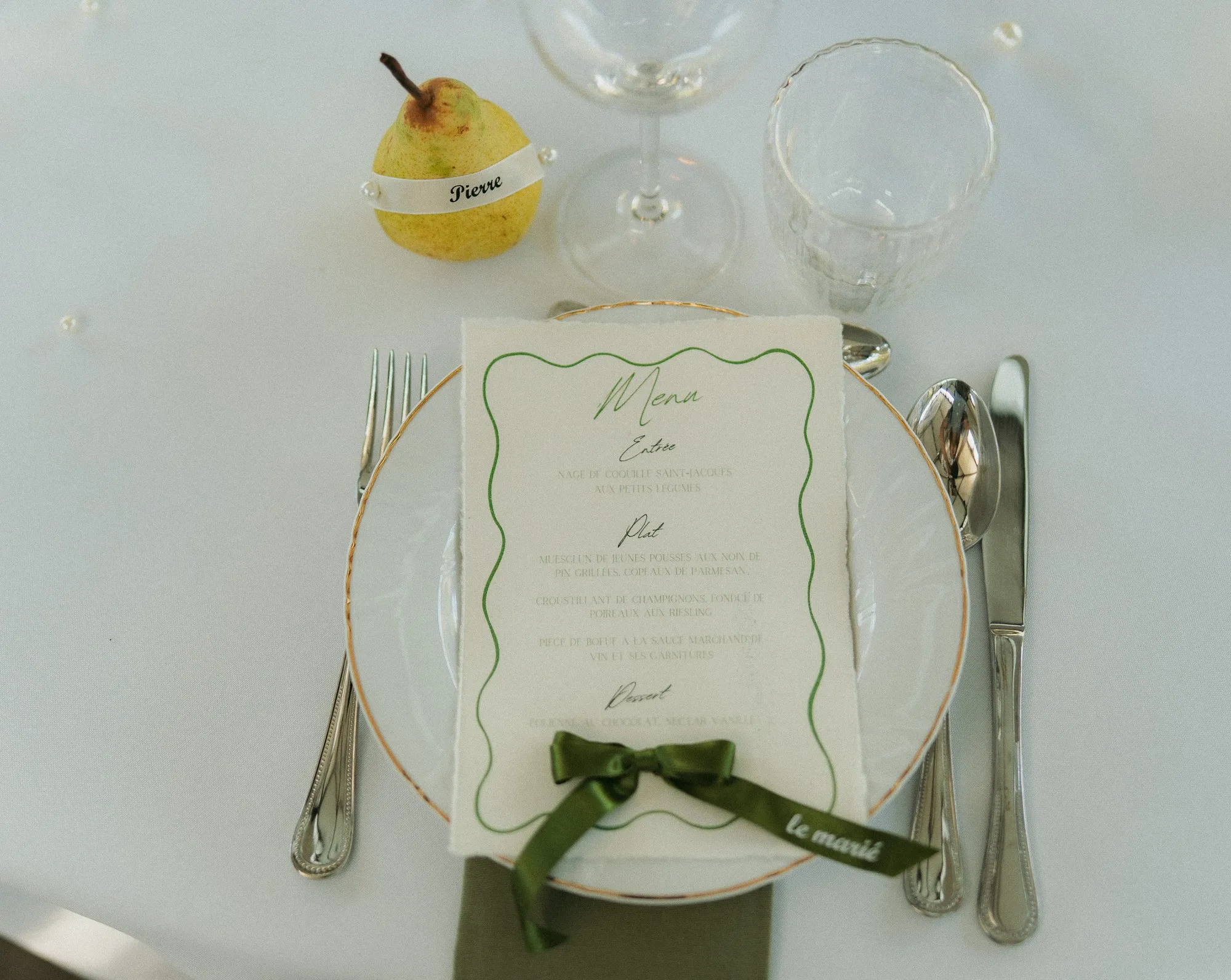Menu calligraphié noué d'un ruban vert, poire marque-place posée au-dessus de l'assiette