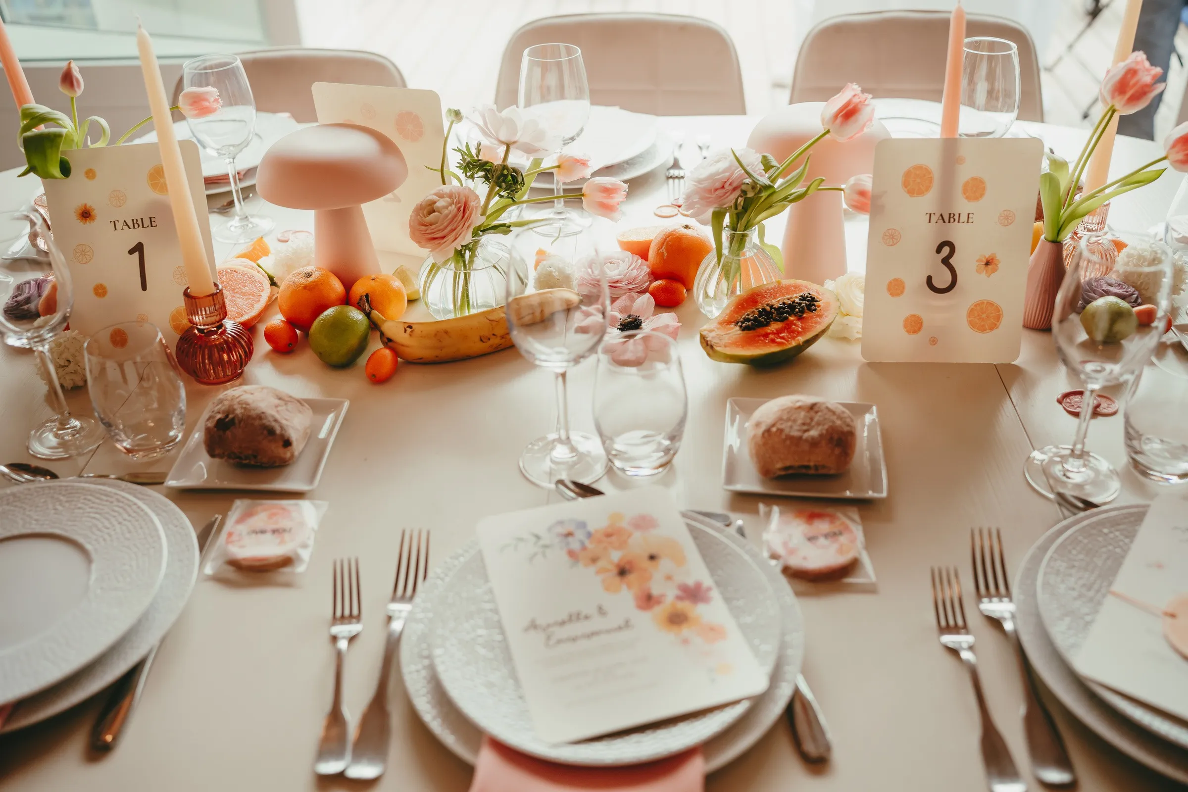 Table du dîner aux couleurs acidulées : agrumes, papaye, bougies roses et numéros de table illustrés