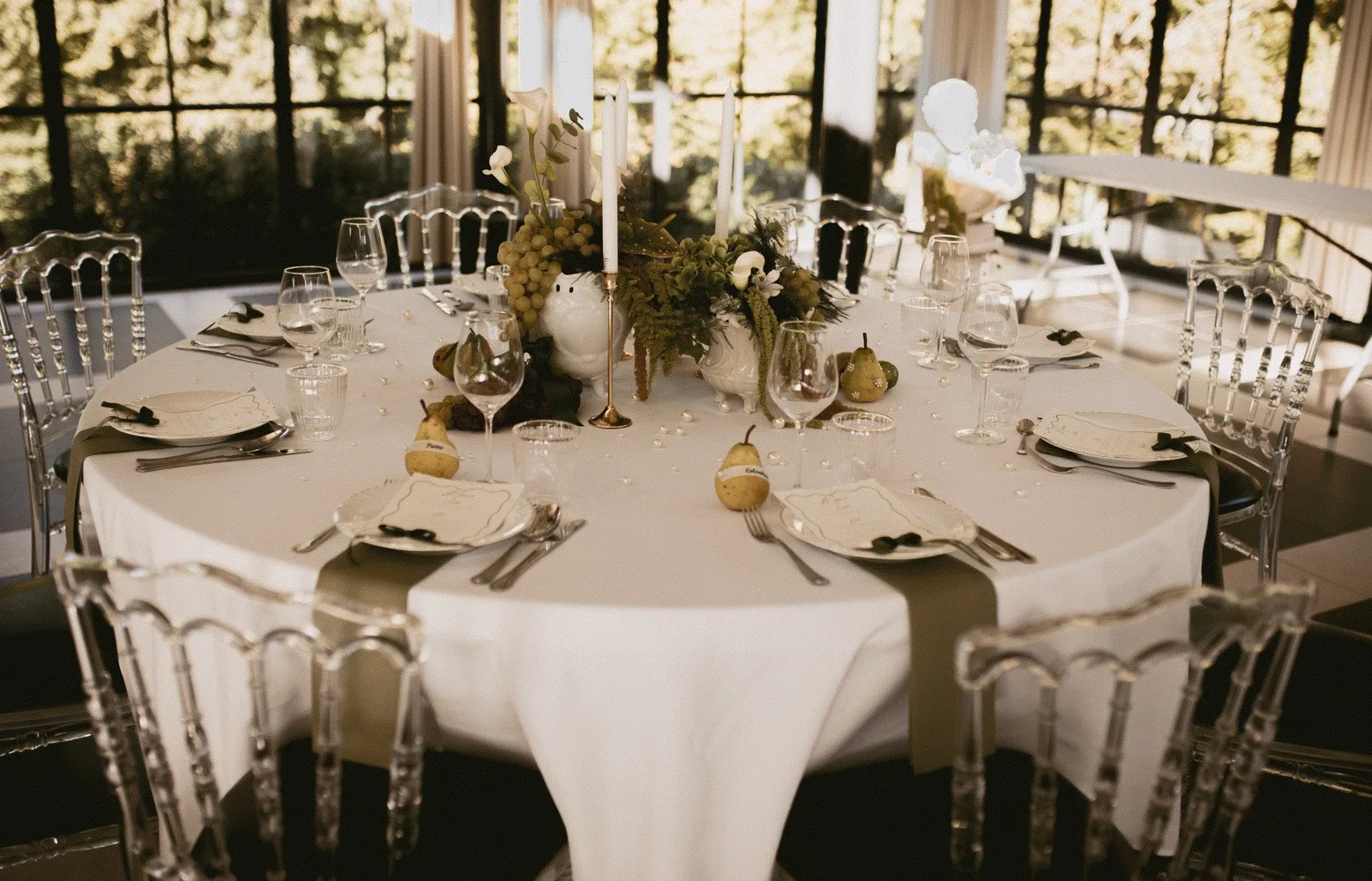 Table ronde dressée sous une verrière, centre de table en raisins, feuillages et bougies