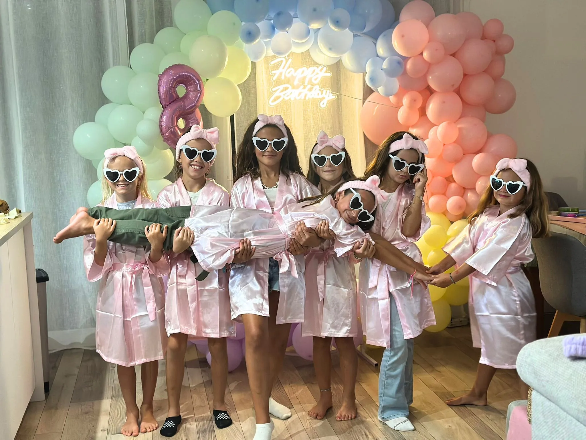 Les invitées en peignoir rose et lunettes cœur devant une arche de ballons